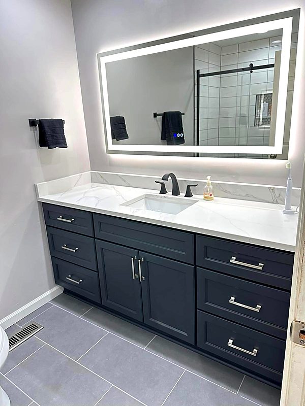 Navy blue bathroom vanity with a quartz top, matching backsplash and a backlit LED mirror