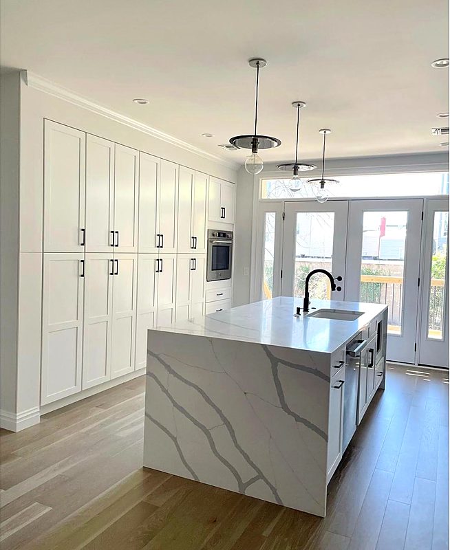 White shaker kitchen with a veined quartz waterfall island and floor-to-ceiling pantry cabinets