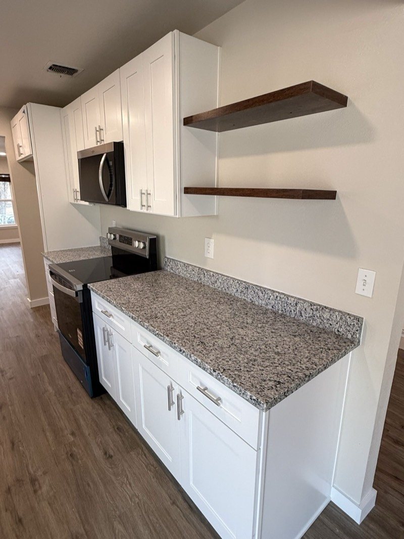 White shaker cabinets with speckled granite and floating wood shelves